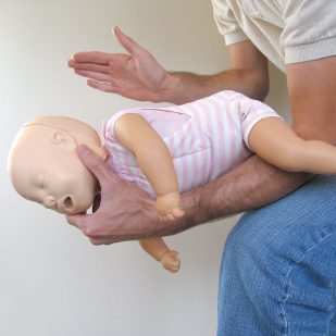 Image shows a person’s arm holding a baby manikin, demonstrating what to do if a baby is choking.